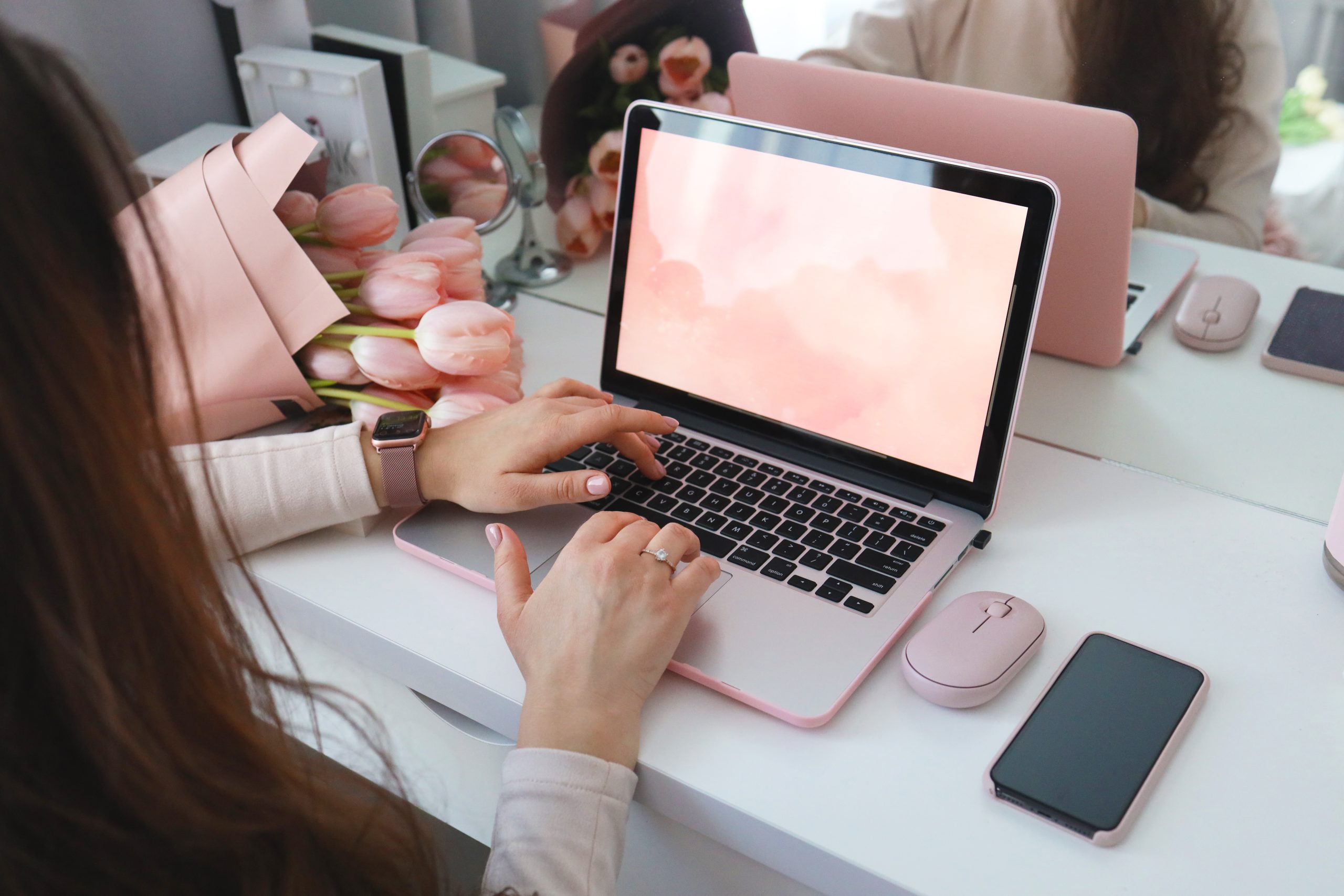 Female hands using laptop. Female office desk workspace homeoffice mock up with laptop, pink tulip flowers bouquet, smartphone and pink accessories.